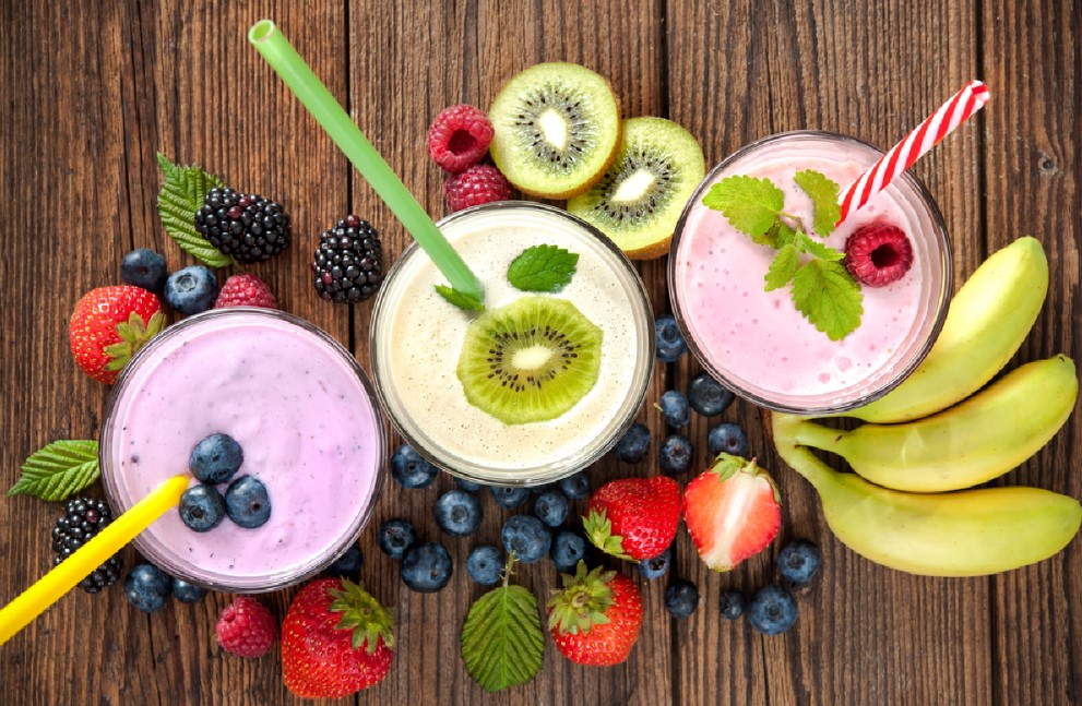 three smoothies with straws surrounded by fruit